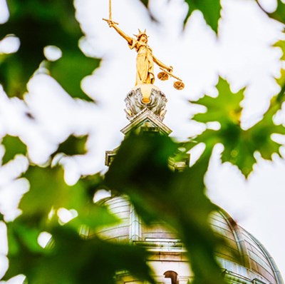 Statue of justice holding a sword in one hand a scales in the other on the dome of the old Baily in London seen through blurred leaves 