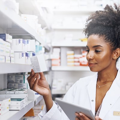 Pharmacist looking at a packet in a room surrounded with medication on shelve 