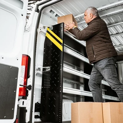 Man in a white van talking a box from a shelf with two more boxes at his feet