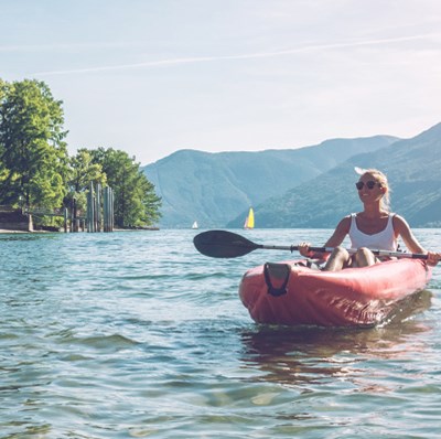 Woman in an inflatable canoe in the water with trees and mountains in the background