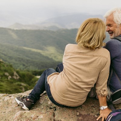 A retirement age couple with rucksacks sitting on a rock with a backdrop of rolling green hills