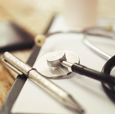 Stethoscope and pen and a blurred mobile on top of a wooden desk 