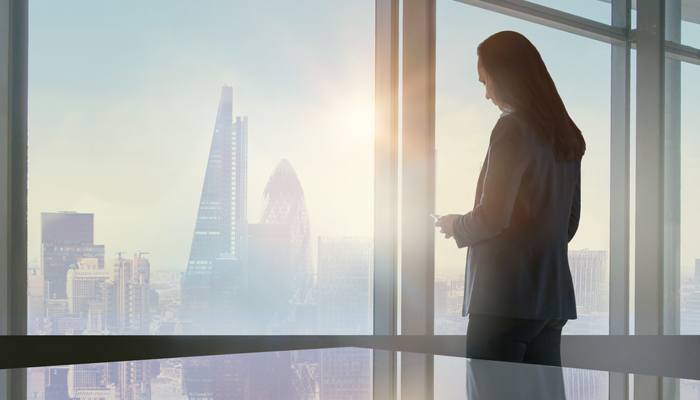 Businesswoman In Office Looking Out Over Commercial Buildings