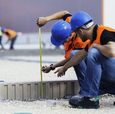 Two men on their hunches in hard hats and high viz measuring the height of construction material above ground level Two men on their hunches in hard hats and high viz measuring the height of construction material above ground level
