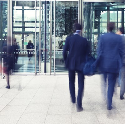 Smartly dressed people walking up to and leaving revolving office doors 