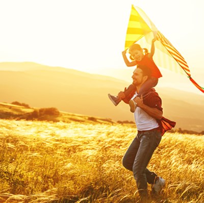 Young boy holding a kite, sitting on the shoulders of his father, walking through a field of corn, a white sky and yellow back drop of fields and hills Young boy holding a kite, sitting on the shoulders of his father, walking through a field of corn, a white sky and yellow back drop of fields and hills