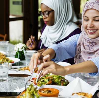 Women in headscarves sitting at a table enjoying sharing plates Women in headscarves sitting at a table enjoying sharing plates