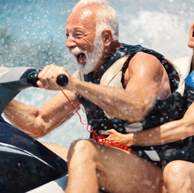 Older man driving a jet ski with an older women riding behind his seat