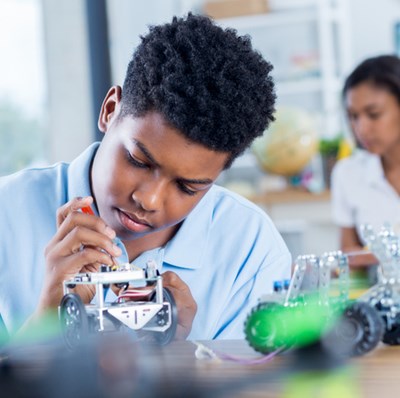Boy working on electronics in a class room with a screwdriver