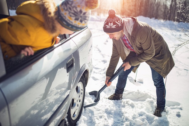 Man digging snow around car while person in car looks on