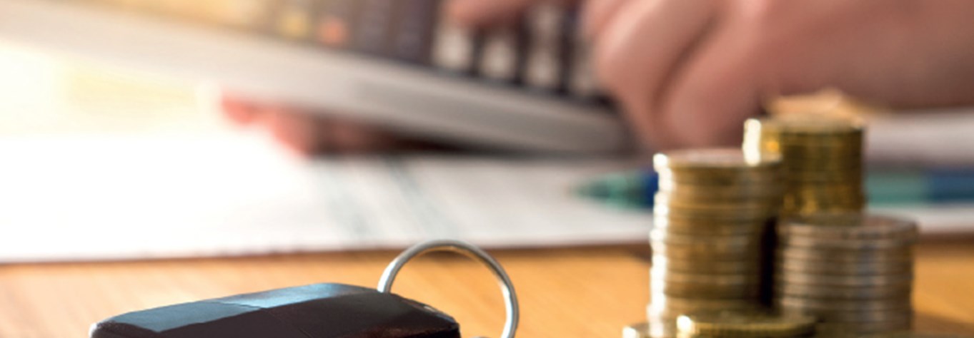 car keys on a desk with a pile of coins and a blurred finger on a calculator