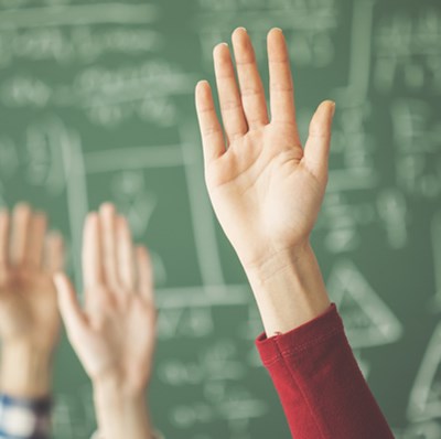 Four hands held up with a blurred background of a green board with white writing lines, triangles and squares Four hands held up with a blurred background of a green board with white writing lines, triangles and squares