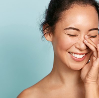 Head and shoulder shot of a smiling women with fingers along the side of her nose and face Head and shoulder shot of a smiling women with fingers along the side of her nose and face