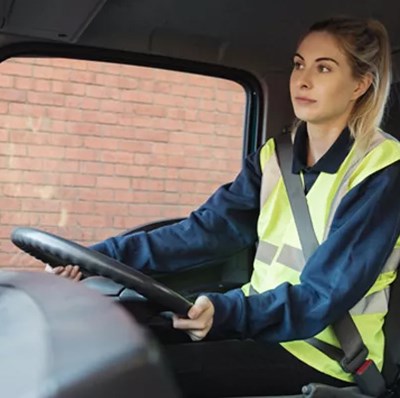 Passenger side view of a women in a hi viz vest sitting behind the steering wheel of a truck