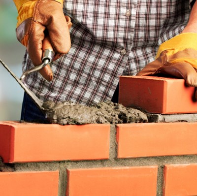 A torso shot of a man wearing a checked shirt and gloves building a wall