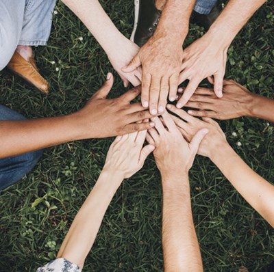 Hands and arms view of people sitting on the grass on a circle with their hands flat palms down touching  Hands and arms view of people sitting on the grass on a circle with their hands flat palms down touching