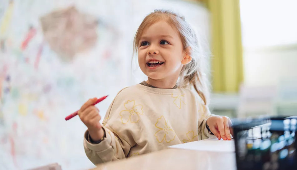 Little girl smiling at nursery with a pen in her hand