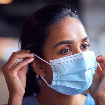 Face shot of a woman in scrubs putting on a surgical mask