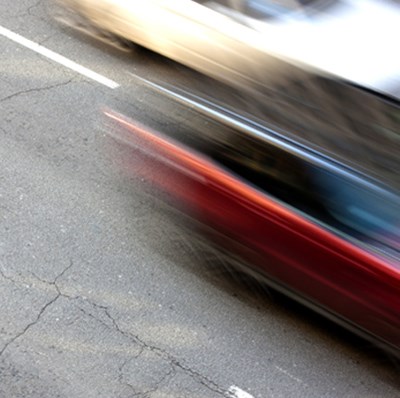 Blurred shot, using a slow shutter speed, viewing from above, the side of two cars driving on a four lane road