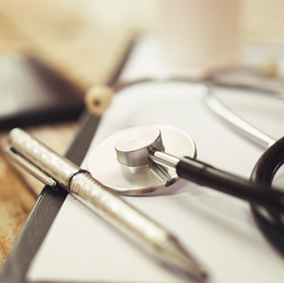 Stethoscope and pen and a blurred mobile on top of a wooden desk  Stethoscope and pen and a blurred mobile on top of a wooden desk