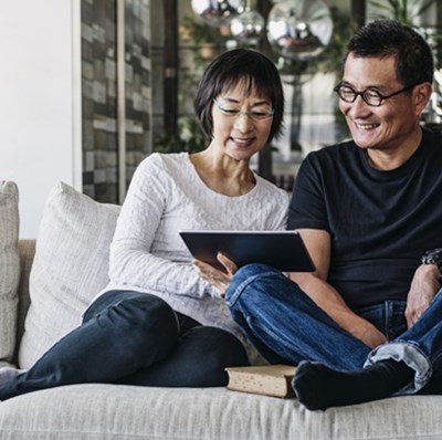 Smiling couple on a sofa looking at a tablet screen being held by the women Smiling couple on a sofa looking at a tablet screen being held by the women