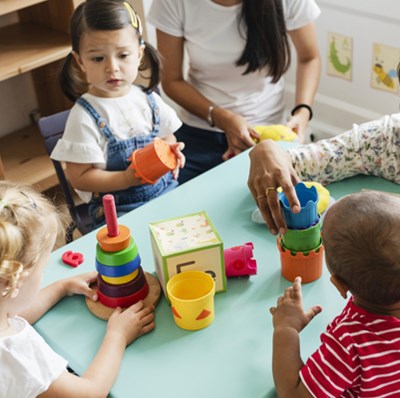 Nursery children playing with simple building blocks on a table with two women Nursery children playing with simple building blocks on a table with two women