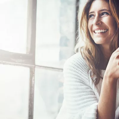 Smiling women with a mug in her hands with her back to a window, looking outside Smiling women with a mug in her hands with her back to a window, looking outside