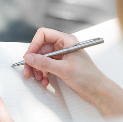 Hand view of a women holding a pen to a page in a note book Hand view of a women holding a pen to a page in a note book