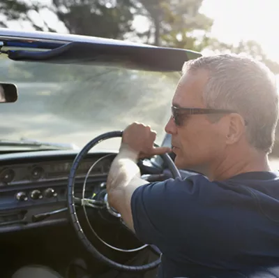 View from the back seat of a greying man driving a classic car with the top down  