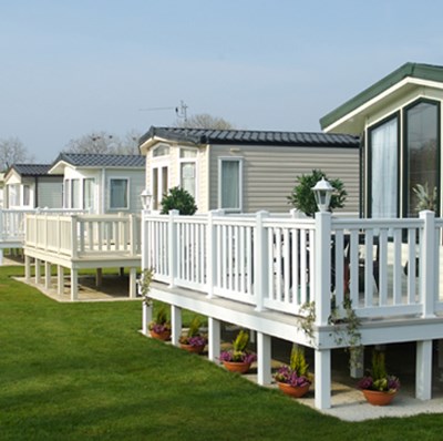 Row of static caravans with fenced raised patios overlooking manicured grass