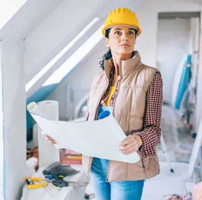 Women wearing a hard hat holding a rolled out architectural blueprint in a loft space in the process of being renovated space  Women wearing a hard hat holding a rolled out architectural blueprint in a loft space in the process of being renovated space