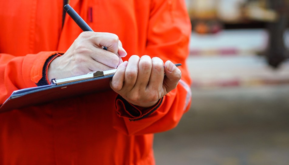 Worker in orange overalls holding clipboard