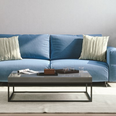 Sofa on with side a board with a lamp on the left, a large cheese plant to the right,  and a coffee table on a rug in front. Sofa on with side a board with a lamp on the left, a large cheese plant to the right,  and a coffee table on a rug in front.