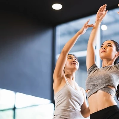 Two women in a dance studio, one with her arms above her head, palms facing, while the other pushes the wrist of that girl Two women in a dance studio, one with her arms above her head, palms facing, while the other pushes the wrist of that girl