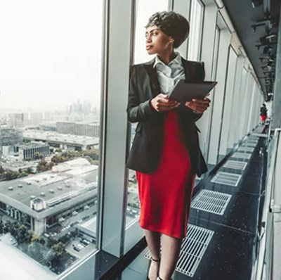 Woman standing by a floor to ceiling window looking out over a city view Woman standing by a floor to ceiling window looking out over a city view