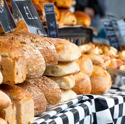 A staked row of various bread types on a chequered clothed table with their prices behind them