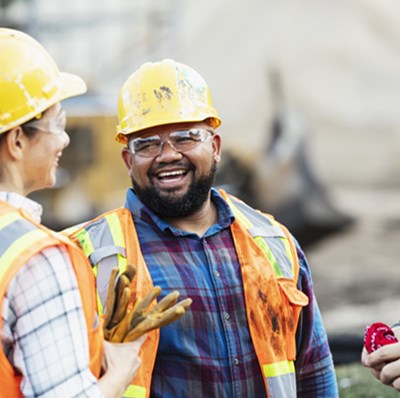 Two men and a women wearing a hard hat, high viz, standing in a circle smiling at each other