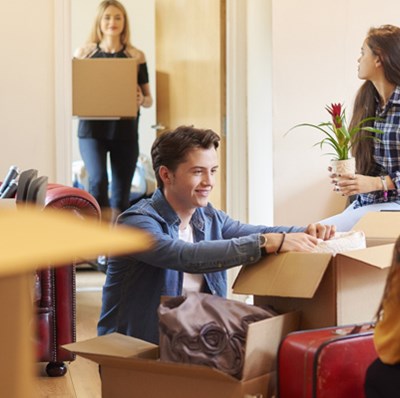 Three young women and a man unpacking boxes in a living room with boxes and soft furnishings Three young women and a man unpacking boxes in a living room with boxes and soft furnishings