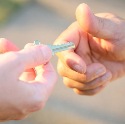 Hand view of a key being past from one to another over a blurred grass edged path Hand view of a key being past from one to another over a blurred grass edged path