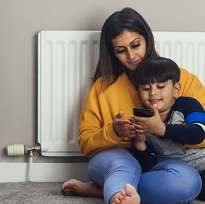 Mother and son sitting next to a radiator looking at the mobile in the boys hands