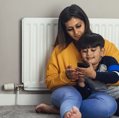 Mother and son sitting next to a radiator looking at the mobile in the boys hands Mother and son sitting next to a radiator looking at the mobile in the boys hands