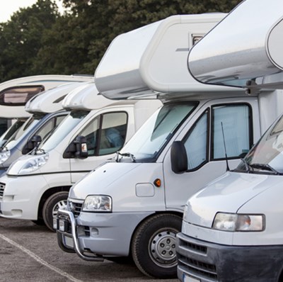 A row of motorhomes in a car park with trees in the background A row of motorhomes in a car park with trees in the background