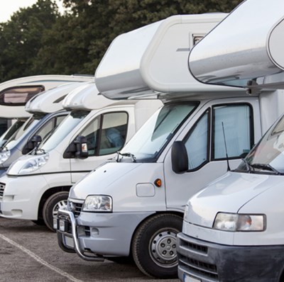 A row of motorhomes in a car park with trees in the background