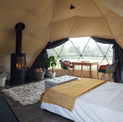The inside of a glamping dome tent with a wood burning stove and view of a field and trees