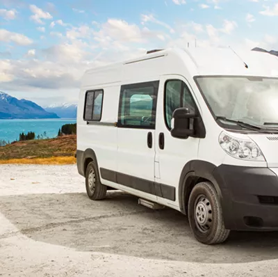 Front and side view of a mini bus parked on concreate with a backdrop of water, mountain, blue sky and white clouds Front and side view of a mini bus parked on concreate with a backdrop of water, mountain, blue sky and white clouds