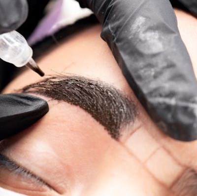 Eyebrow being microbladed by hands in black surgical gloves  