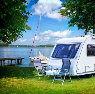 Touring caravan parked beside a tranquil lake, surrounded by greenery, in a peaceful atmosphere  Touring caravan parked beside a tranquil lake, surrounded by greenery, in a peaceful atmosphere
