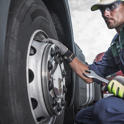 Man with wearing protective glasses and clothing, holding a spanner and crouched by a truck wheel