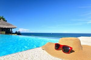 Holiday photo of hat and sunglasses by an outdoor swimming pool