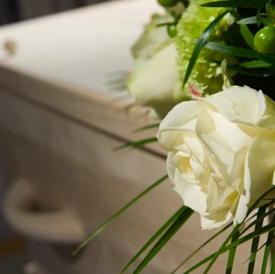 A blurred backdrop of a wooden coffin and curtains with with roses, green carnations, green berries and fern greenery in focus on top  A blurred backdrop of a wooden coffin and curtains with with roses, green carnations, green berries and fern greenery in focus on top